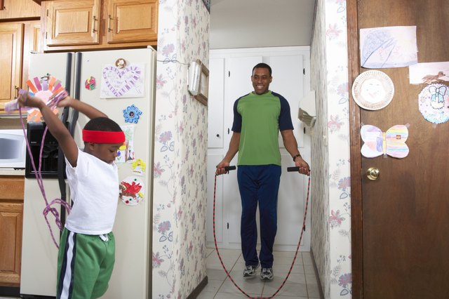 Father and son (4-5) exercising with skipping rope in house