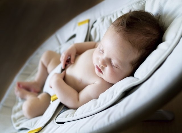 Newborn baby girl sleeping on bouncer chair in dark room