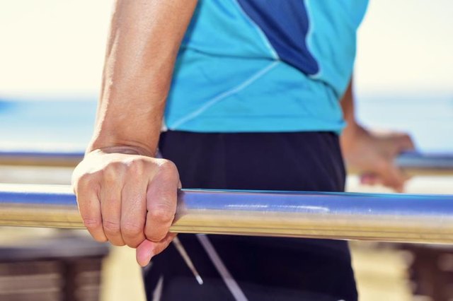 closeup of a young caucasian sportsman wearing sport clothes doing doing dips in parallel bars outdoors