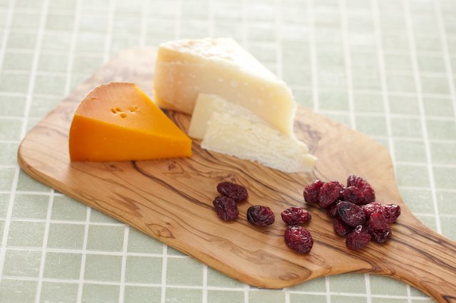 A cutting board with different kinds of cheese and dried fruit