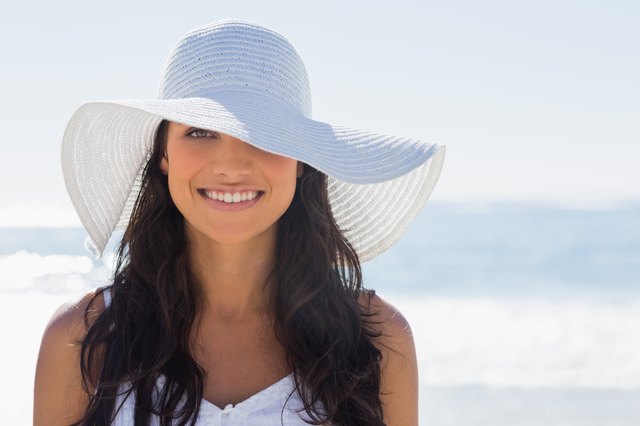 Pretty brunette in white sunhat smiling at camera