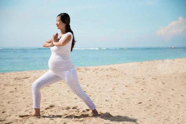 Pregnant asian woman doing yoga in the sea shore