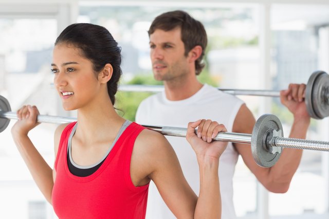 Fit young couple lifting barbells in gym