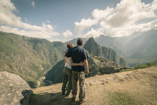 Hugging couple standing in contemplation on the terraces above Machu Picchu, the most visited travel destination in Peru. Rear view, toned, desaturated and vintage styled image.