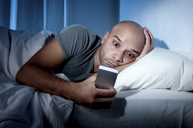 young cell phone addict man in bed using smartphone