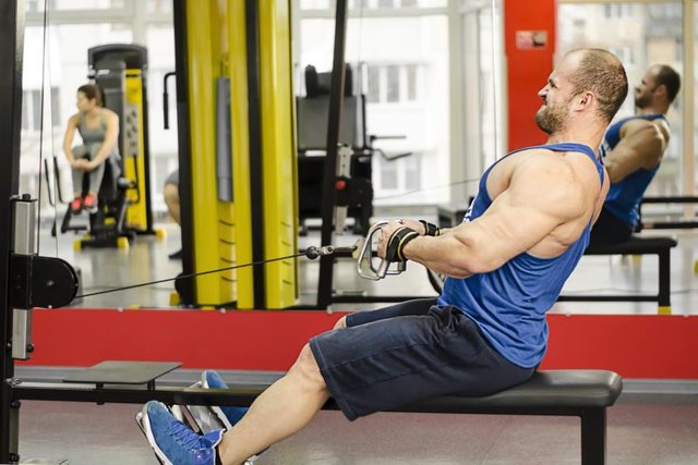 Young male with strained face doing cable row exercises, guy building muscles