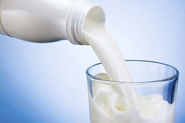 Pouring milk from white plastic bottle into glass on blue