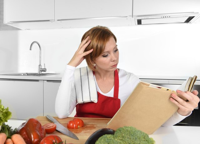 young beautiful home cook woman in kitchen reading cookbook