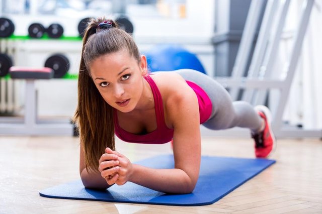 Cute, healthy, young athlete girl in sportswear while planking on a mat at the gym, expressing wellbeing and fitness.