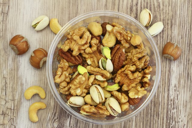 Selection of mixed nuts in plastic box on wooden surface