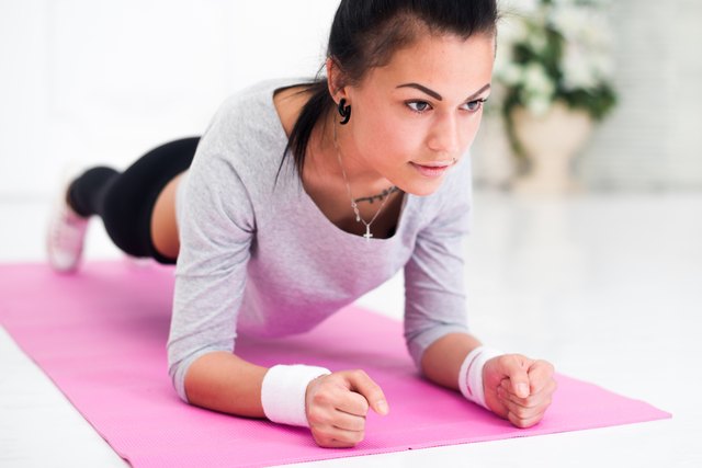 Pretty young woman doing plank abdominal exercise at home in