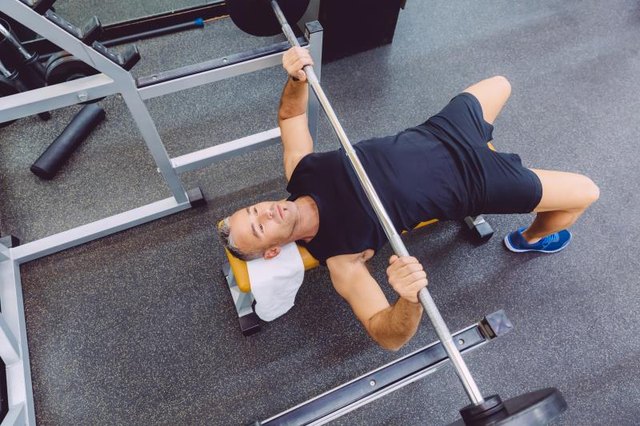 Handsome man doing exercises with barbell on a bench press training in a fitness center