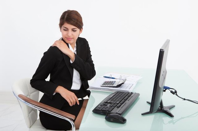 Young businesswoman having shoulder pain while working at computer desk in office