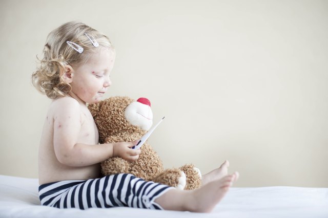 Sick girl is sitting on the bed with teddy-bear