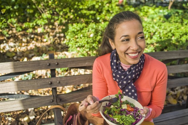 Young woman sitting on park bench eating lunch