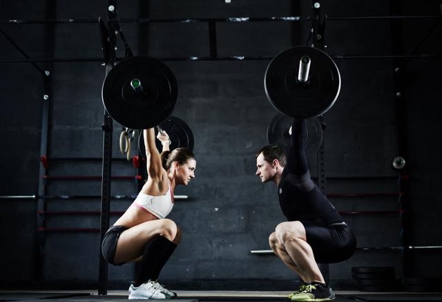 Active young man and woman lifting heavy barbells opposite one another