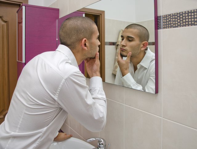 Handsome young man looking at himself in bathroom mirror
