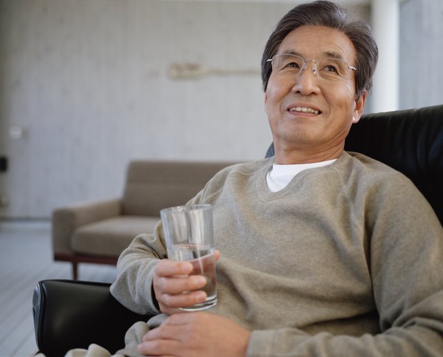 Senior man sitting on armchair holding glass of water, looking up
