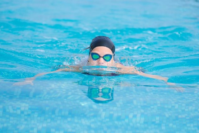 Young girl in goggles and cap swimming butterfly stroke style in the blue water pool