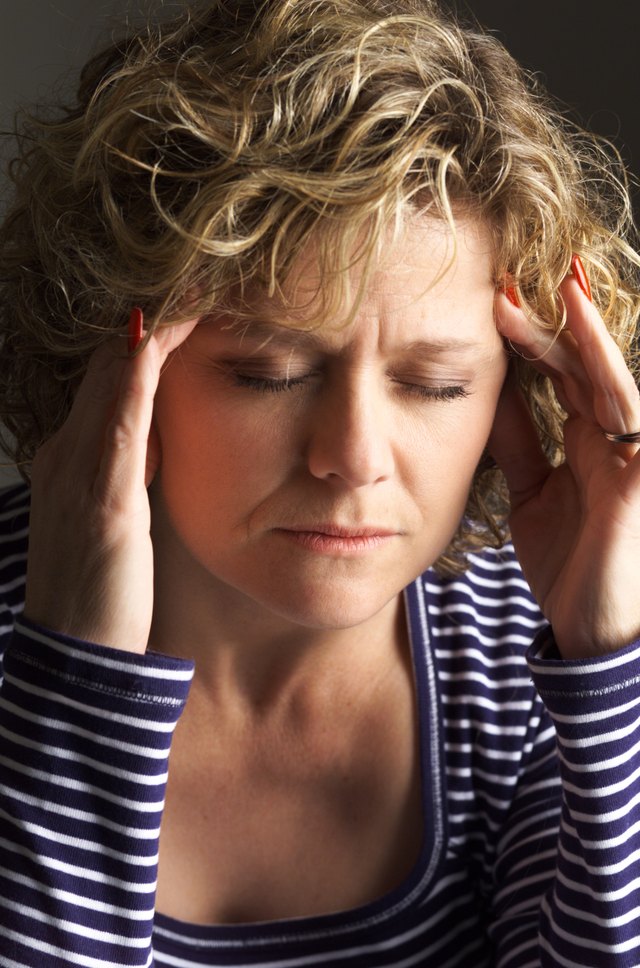 a middle aged caucasian woman in holding her temples and closing her eyes as if in pain