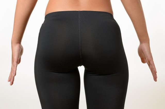 Toned buttocks and thighs of a shapely young woman holding her hands away from her sides isolated on white, close up view