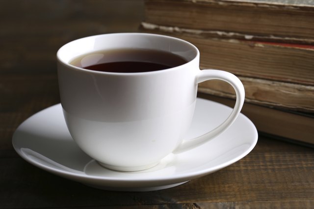 Cup of hot tea with books on table close up