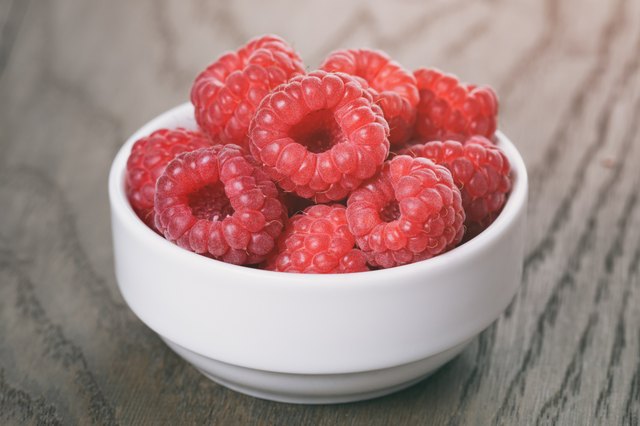 raspberries in white bowl on wood table