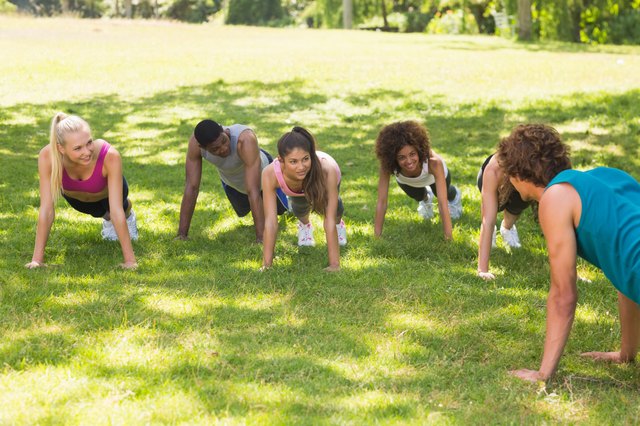 Instructor with fitness class doing push ups in park