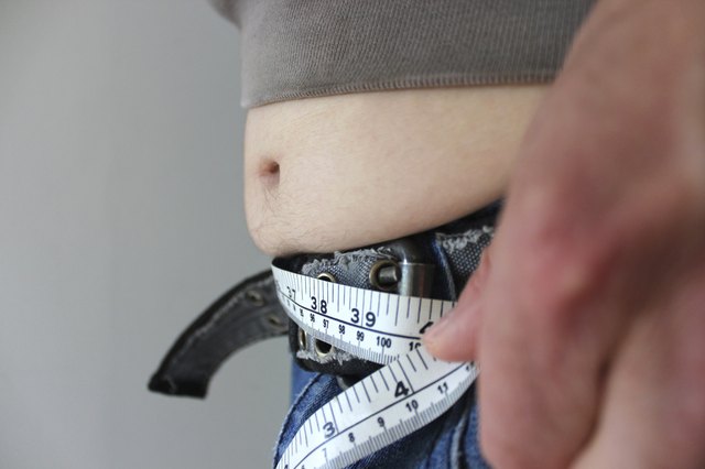 Overweight man with a fat tummy spilling over jeans, measuring