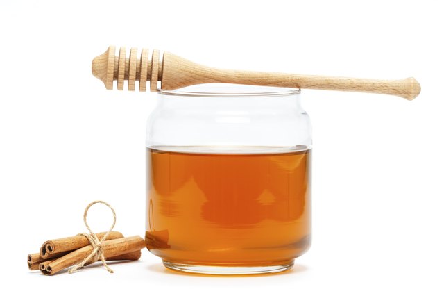 Honey in jar with dipper and cinnamon on isolated background