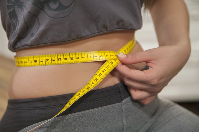 Unrecognizable woman measuring her waist with tape measure.