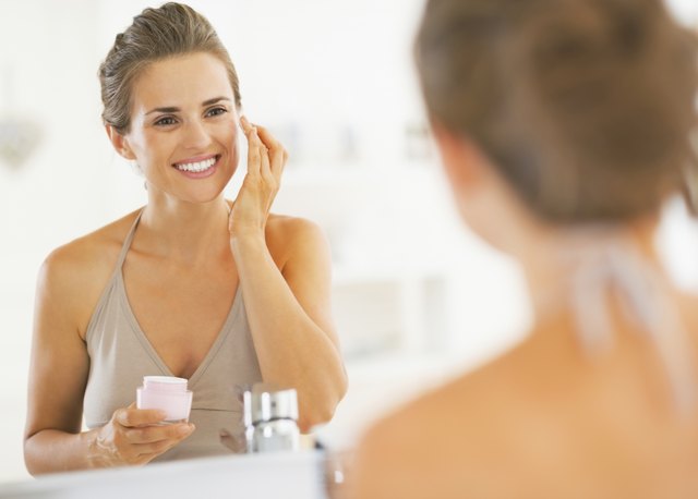happy young woman applying cream in bathroom