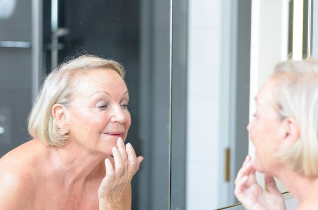 Senior lady checking her skin in the mirror