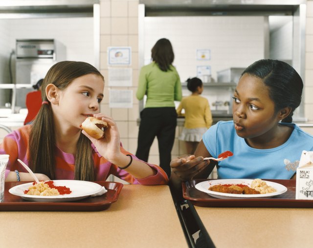 Two Schoolgirls Sitting at a Table in a Canteen Eating Their Lunch