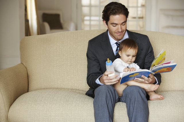Father reading to daughter (15-18 months) on sofa