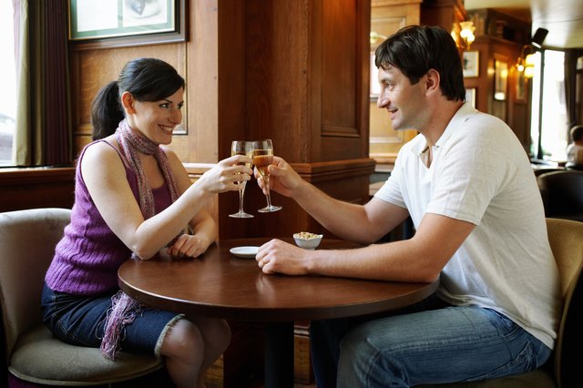 Couple sitting at table in bar, toasting with champagne, smiling