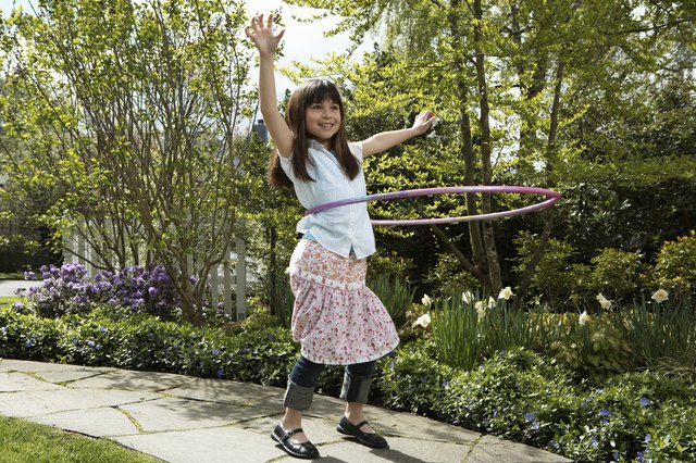 Girl (8-10) playing with plastic hoop, arms raised, smiling
