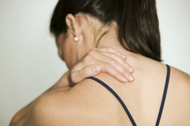 Woman massaging shoulder, in studio, rear view