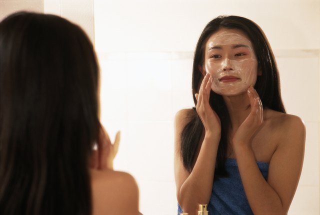 Young woman applying moisturizer on face
