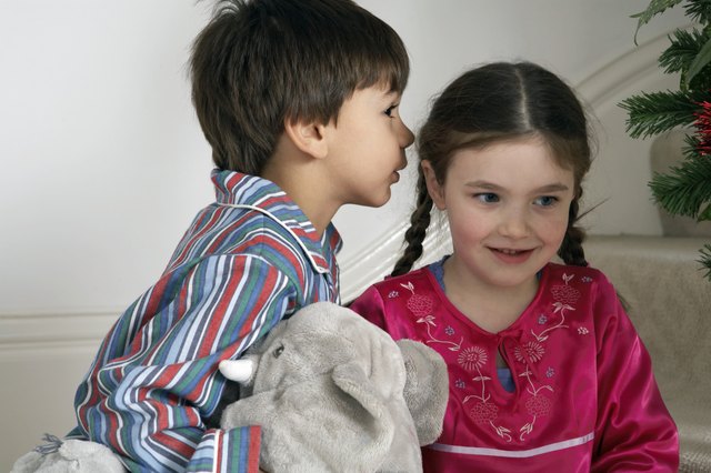 Girl and boy (5-7) sitting on stairs, boy whispering to girl