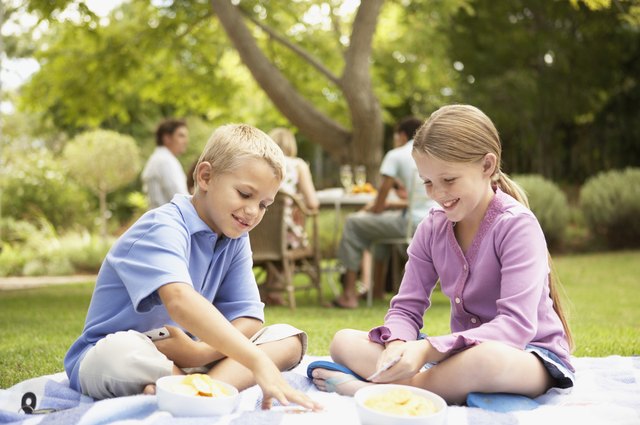 Young Boy and Girl Sit on a Rug in Their Garden Playing a Game of Cards