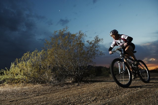 Female rider mountain biking on dirt track at dusk