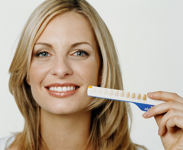Woman holding up tooth whitening chart, smiling, portrait, close-up