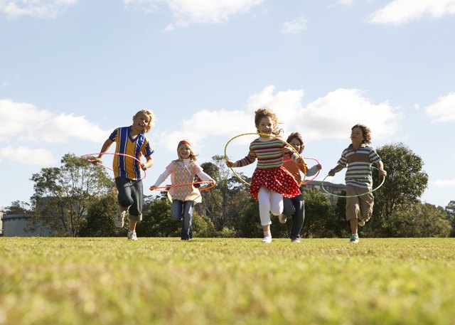 Five children (7-11) running with plastic hoops in park (surface level)