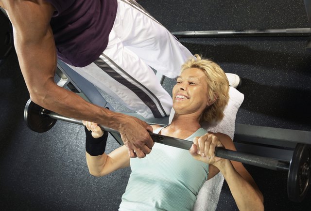 Mature woman lifting weight guided by male instructor, smiling