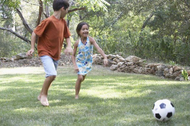 Front profile of a boy and a girl playing football in a garden