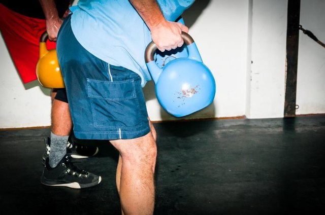 Intensive fitness training. Side view of young man in sportswear working out with kettle bell at gym. Selective focus, real time workout, no posing.