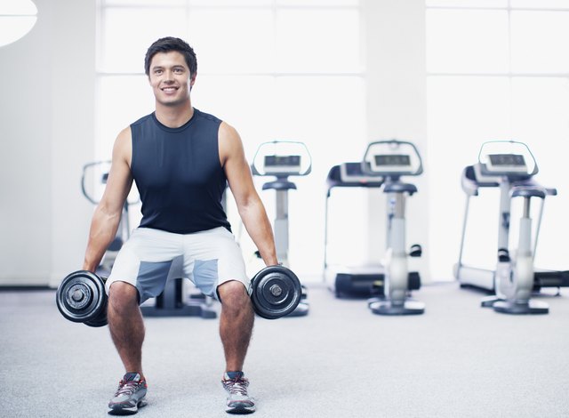 Smiling man doing squats with dumbbells in gymnasium