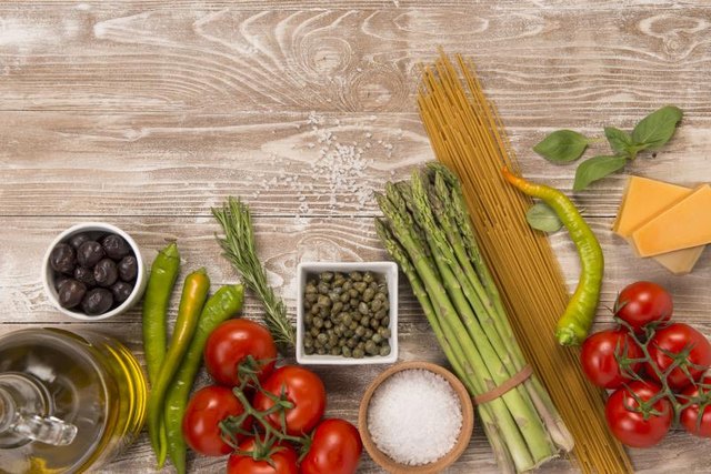 Fresh vegetables, parmesan cheese, olive oil, pasta and olives on wood surface