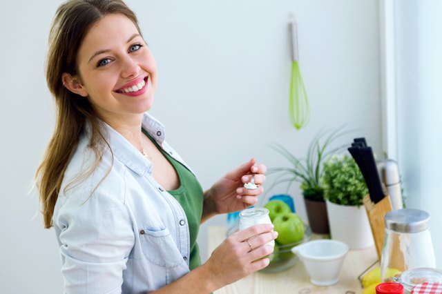 Pretty young woman eating yogurt in the kitchen.